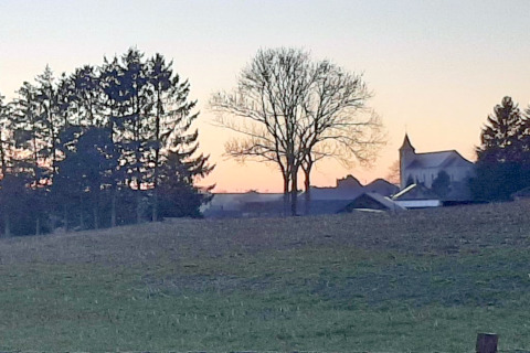 Zonsondergang over een groene weide met bomen en een kerk, gezien vanaf een glampingverblijf.