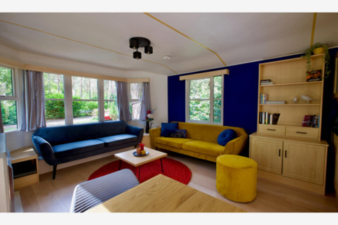 Soggiorno della lodge Sijs in Belgio con divani blu e giallo, parete blu e grandi finestre luminose.