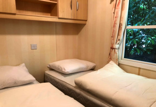 Due letti singoli in una piccola stanza del lodge Sijs in Belgio, con finestra e mobili in legno chiaro.