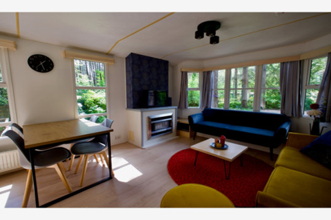 Coin salon lumineux dans le lodge Sijs en Belgique, avec canapés modernes, table à manger et fenêtres.