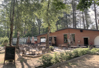 Area glamping all’aperto con tavoli e sedie davanti a una struttura in mattoni, circondata da alberi.