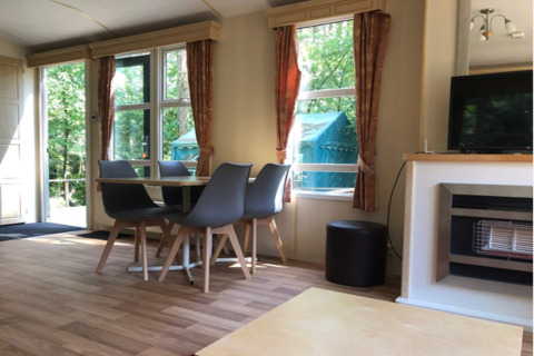 Vue intérieure d’un lodge lumineux «Sijs» avec coin repas et grandes fenêtres donnant sur la nature en Belgique.