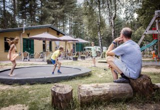 Un homme regarde des enfants jouer sur un trampoline près d’un hébergement glamping en pleine nature.