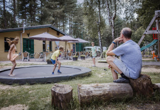 Un homme regarde des enfants jouer sur un trampoline près d’un hébergement glamping en pleine nature.