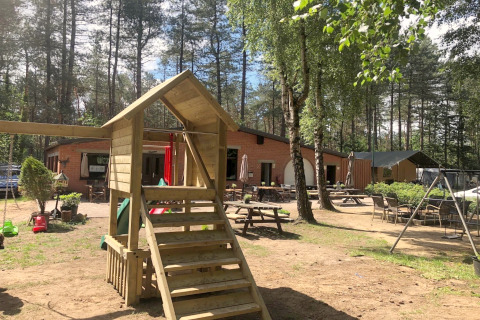 Area giochi e posti a sedere in una sistemazione glamping circondata da boschi e alberi in una giornata di sole.