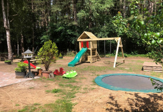 Area giochi in una sistemazione glamping con scivoli, altalene, trampolino e verde circostante.