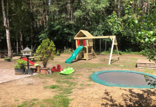 Udendørs legeplads ved et glampingsted med rutsjebaner, gynger, trampolin og grønne omgivelser.