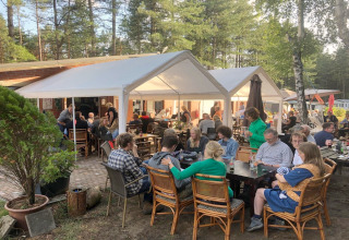Repas en plein air dans un hébergement glamping, convives sous des tentes, entourés de forêt et nature.
