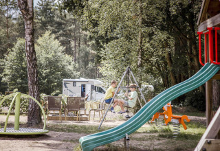 Bambini che giocano in un parco giochi vicino a un'area glamping con camper sullo sfondo in mezzo alla natura.