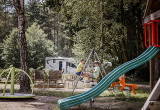 Bambini che giocano in un parco giochi vicino a un'area glamping con camper sullo sfondo in mezzo alla natura.