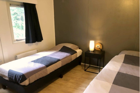 Gezellige kamer in lodge 'Ekster' in België met twee single bedden, nachtkastje en raam met gordijn.