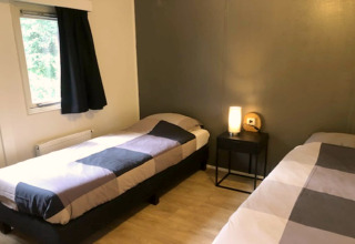 Chambre confortable au lodge 'Ekster' en Belgique avec deux lits simples, table de nuit et fenêtre avec rideau.