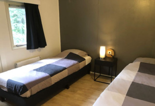 Camera accogliente al lodge 'Ekster' in Belgio con due letti singoli, comodino e finestra con tenda.