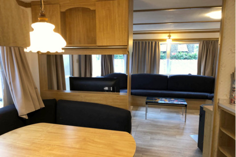 Vue intérieure du chalet Specht en Belgique avec table à manger, canapés, rideaux et décor en bois.