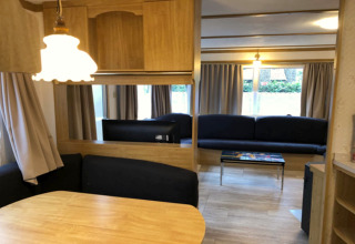 Vue intérieure du chalet Specht en Belgique avec table à manger, canapés, rideaux et décor en bois.
