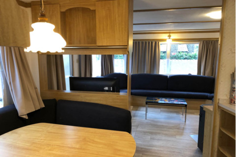 Vue intérieure du chalet Specht en Belgique avec table à manger, canapés, rideaux et décor en bois.