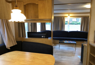Vue intérieure du chalet Specht en Belgique avec table à manger, canapés, rideaux et décor en bois.
