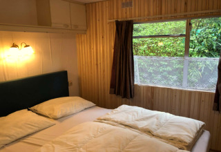 Chambre douillette au chalet Specht en Belgique, lit double, murs boisés et vue sur la verdure extérieure.