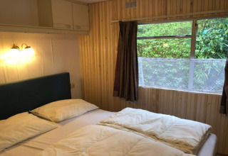 Et hyggeligt soveværelse med dobbeltseng, træpaneler og udsigt til grøn have på chalet Specht i Belgien.
