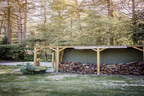Foto van een houthok met stapels brandhout, midden in het bos, genomen bij een glampingverblijf.