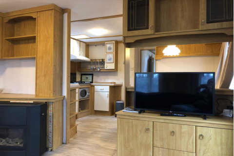 Stueområde i chalet Specht, Belgien, med moderne træinteriør, TV, køkken og hyggelig belysning.