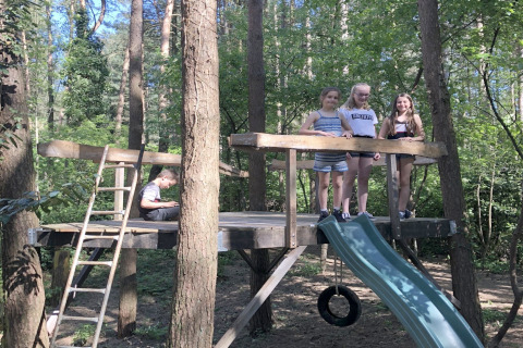 Kinderen spelen op een boomhut met glijbaan en ladder aan chalet 'Specht' in het Belgische bos.