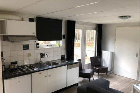 Modern lodge kitchen and living area in Belgium with white cabinets, chairs, and forest view outside.