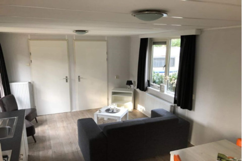 Interior photo of a cozy living space at Koolmees lodge in Belgium, featuring a sofa and windows.