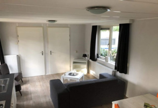 Interior photo of a cozy living space at Koolmees lodge in Belgium, featuring a sofa and windows.