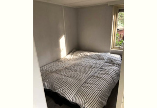 Piccola camera da letto al lodge 'Koolmees' in Belgio, con letto matrimoniale e finestra sul giardino.