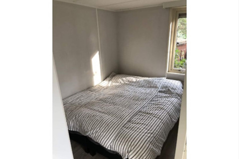 Petite chambre à la lodge «Koolmees» en Belgique, avec lit double, drap rayé et fenêtre sur le jardin.
