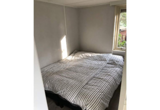 Small bedroom at 'Koolmees' lodge in Belgium, featuring a double bed, striped bedding, and a window.