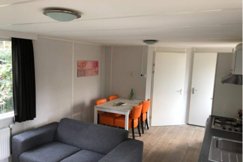 Soggiorno nel lodge Koolmees in Belgio con divano grigio, tavolo da pranzo e sei sedie arancioni.