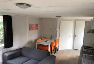 Living room inside Koolmees lodge in Belgium with grey sofa, dining table, orange chairs and kitchen.