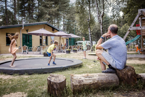 Man kijkt toe hoe kinderen springen op een trampoline bij een lodge met terras in het bos.