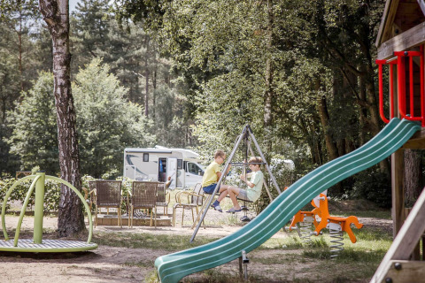 Due bambini giocano sulle altalene in un parco giochi vicino a un camper e delle sedie all'aperto.
