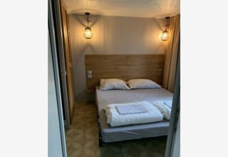Gemütliches Schlafzimmer mit Doppelbett, Holzkopfteil und Lampen in der Sparrowhawk-Lodge in Belgien.