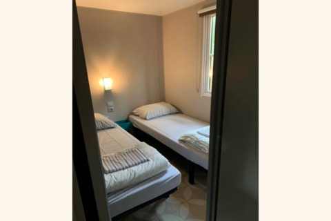 Petite chambre avec deux lits simples, oreillers rayés et lampe murale au Sparrowhawk Lodge en Belgique.
