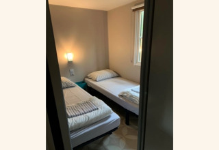 Kleine kamer met twee aparte bedden, wit beddengoed en raam in Sparrowhawk Lodge, België.