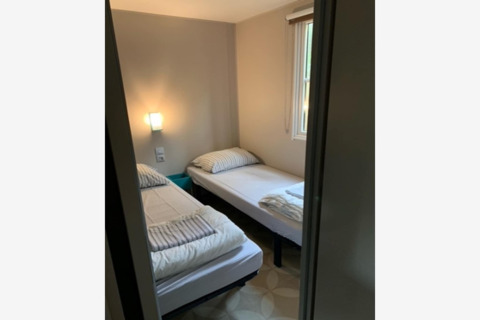 Kleines Zimmer mit zwei Einzelbetten, schlichter Einrichtung und Fenster im Sparrowhawk Lodge, Belgien.