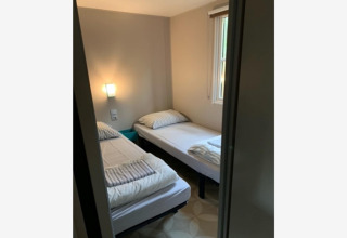 Kleines Zimmer mit zwei Einzelbetten, schlichter Einrichtung und Fenster im Sparrowhawk Lodge, Belgien.