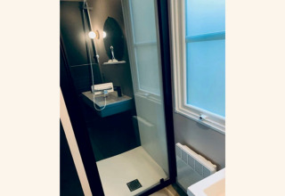 Moderne douche met glazen deur, ronde spiegel en matglas raam in het Sparrowhawk lodge in België.