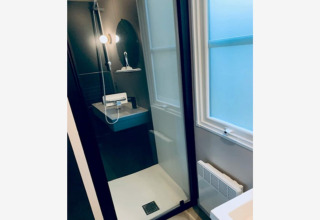 Moderne bruser med glasdør, sort panel og rund spejl på væggen i Sparrowhawk lodge i Belgien.