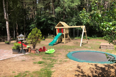 Buitenspeeltuin bij lodge Sparrowhawk in België met glijbaan, schommels en trampoline in het bos.