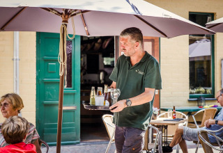Een kelner schenkt drankjes uit op het terras van lodge Sparrowhawk in België, gasten zitten ontspannen.