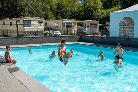 Kinderen spelen in een buitenzwembad voor lodges op een zonnige dag bij een vakantiepark of lodge.