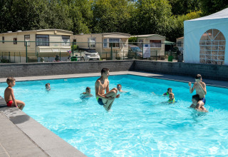 Kinderen spelen in een buitenzwembad voor lodges op een zonnige dag bij een vakantiepark of lodge.