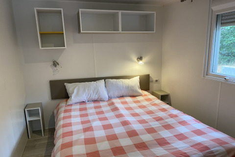 Camera da letto al Verblijfpark Breebos 2 in Belgio con copriletto a quadretti, mensole e finestra.