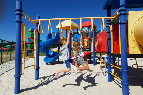 Twee kinderen spelen op een kleurrijke speeltuin met glijbanen en klimrekken onder een blauwe lucht.