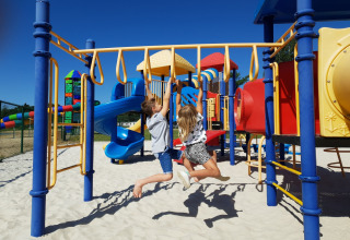 Due bambini giocano su un colorato parco giochi con scivoli e strutture da arrampicata sotto cielo blu.